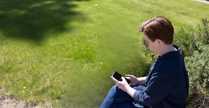 kikker ned på mobilen mens hun sitter på gresset 