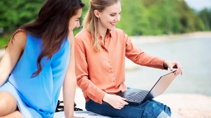 two women sitting near water with laptop