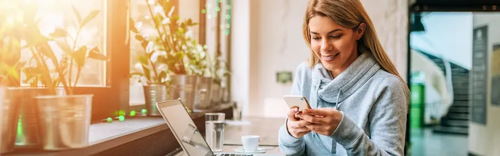 Kvinne smilende ved et bord ser på telefonen sin 